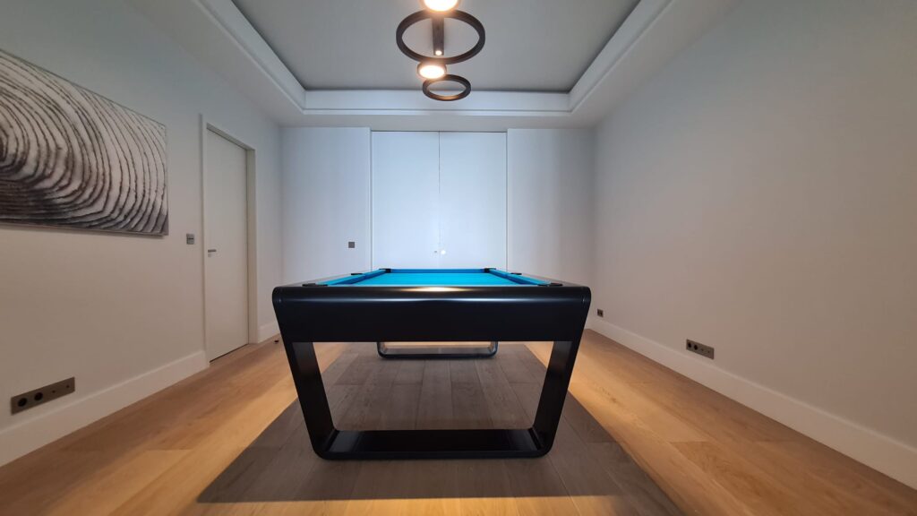 Black luxury pool table with blue felt in a modern minimalist room.