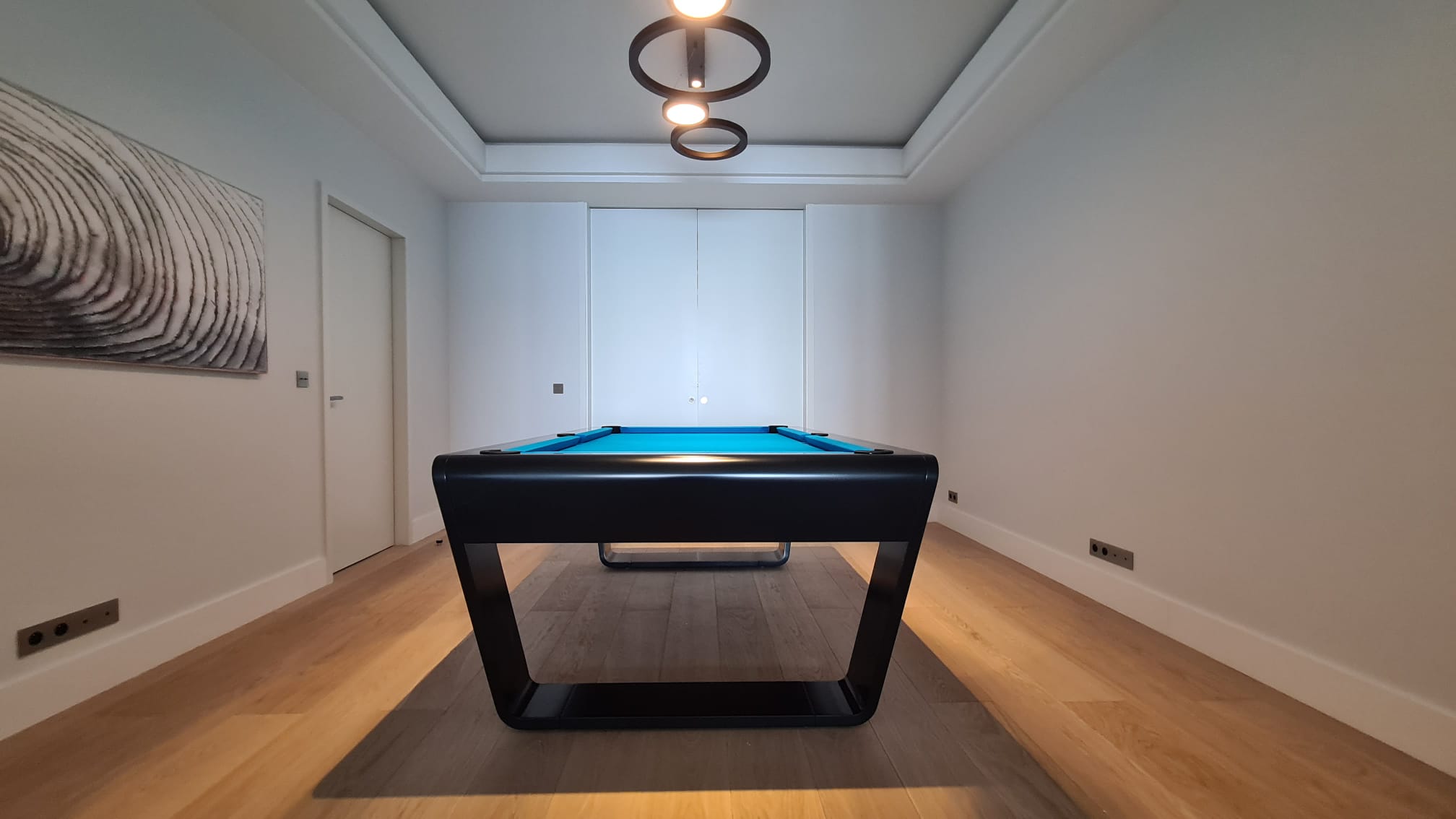 Black luxury pool table with blue felt in a modern minimalist room.