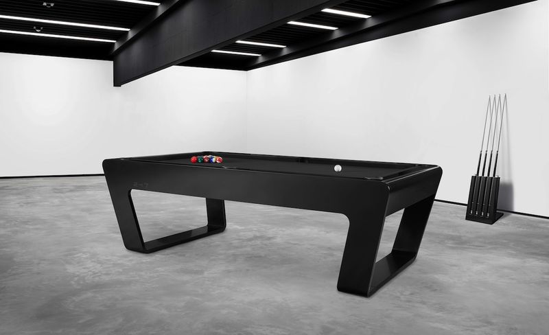 Black luxury pool table with billiard balls and cue rack in a modern industrial interior.
